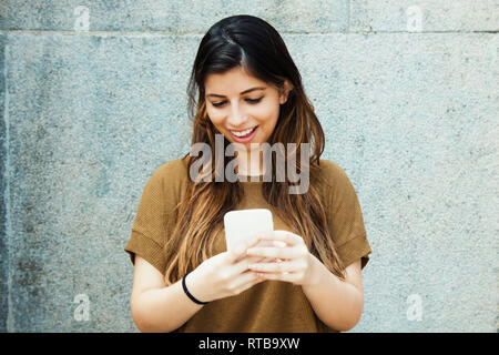 Beautiful latin american young adult woman sending message with mobile phone outdoors in summer Stock Photo