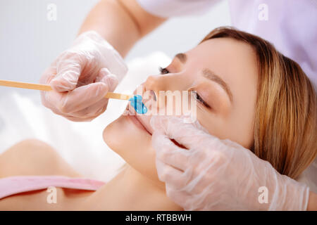 Woman feeling sacred of pain during wax depilation of face Stock Photo