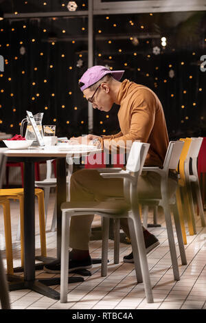 Distantly mulatto man working hard at laptop in diner. Stock Photo