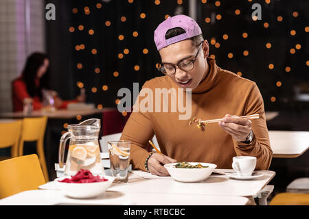 Customer feeling unhappy about ordered dish in restaurant and holding it with chopsticks. Stock Photo