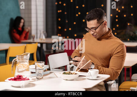 Man refusing to eat ordered dinner and chatting in the smartphone while sitting. Stock Photo