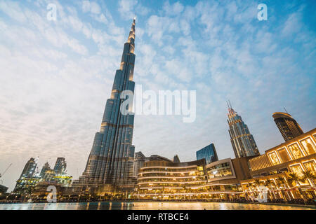 From below blue sky with white clouds over illuminated contemporary skyscrapers on street of Dubai Stock Photo