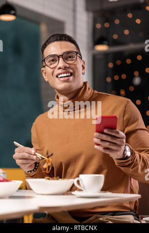 Friends at the next table calling man who eating noodles and typing on the phone. Stock Photo