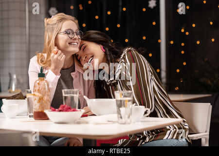 Two young women treating to each other with tenderness while meeting in eating house. Stock Photo