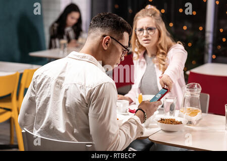Girl trying to take the phone away from her boyfriend to stop his chatting on date. Stock Photo