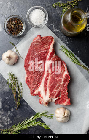 Fresh prime beef steak on white craft paper with rosemary, cardamon, garlic, olive oil, salt and pepper on black background. Concept of fresh healthy  Stock Photo