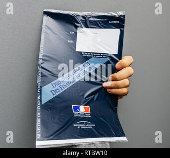 PARIS, FRANCE - OCT 4, 2017: Man holding against gray background envelope containing Taxe d'habitation (rates, property tax) which is sent once per year to very household owner or people who rent a house apartment Stock Photo