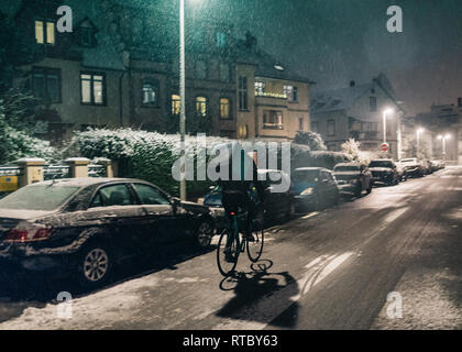 STRASBOURG, FRANCE - DEC 3 2017: Cinematic Deliveroo delivery bike in French city cycling fast for food delivery on time on a cold winter snowy night in residential neighborhood with cars parked Stock Photo