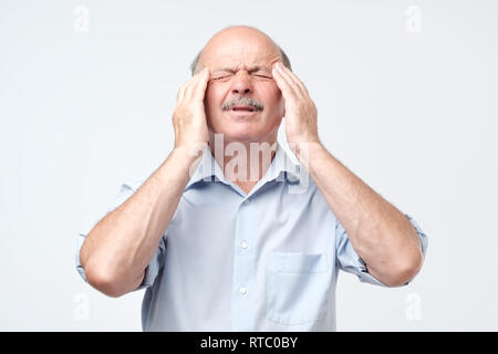 Mature caucasian man isolated on gray background in white casual t-shirt, holding head with both hands, suffering from severe headache or external psy Stock Photo