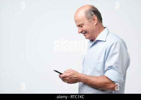 Senior bald man looking at mobile phone. Aside view. Looking photos on blog. Stock Photo