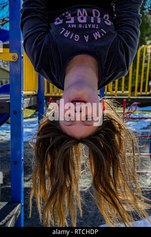 Girl hanging upside down on playground bars Stock Photo