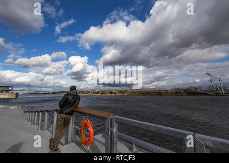 MONTREAL, CANADA - NOVEMBER 7, 2018: Man standing watching Saint Lawrence river in Montreal, Quebec. Pont Jacques Cartier Bridge is visible in backgro Stock Photo