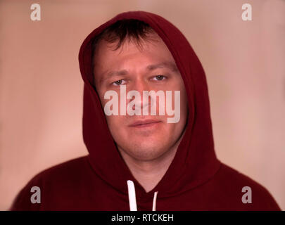 Portrait of a serious young man in a hood on a light background, look into the camera, close-up Stock Photo