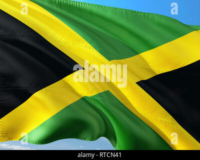 Flag of Jamaica waving in the wind against deep blue sky. High quality fabric. Stock Photo