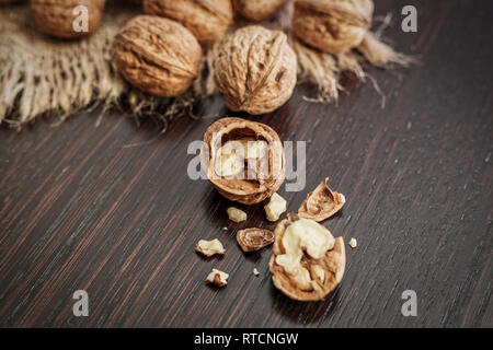 Close-up view of walnut kernels and whole walnuts scattered on a dark wooden table with rustic background, selective focus. Healthy food concept. Stock Photo