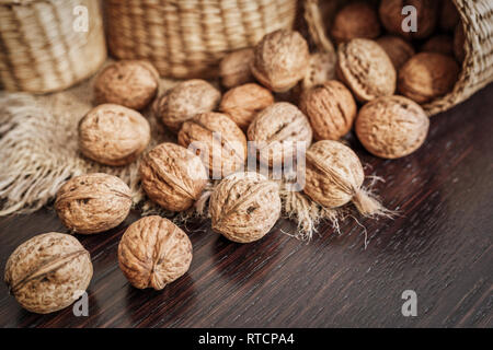 Close-up view of whole walnuts scattered on a dark wooden table with rustic background, selective focus. Healthy food concept. Stock Photo