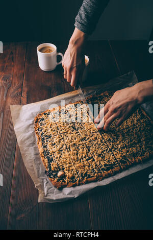 View from above woman's hands cutting freshly baked viennese cookies next to two cups of coffee on brown wooden table. Stock Photo