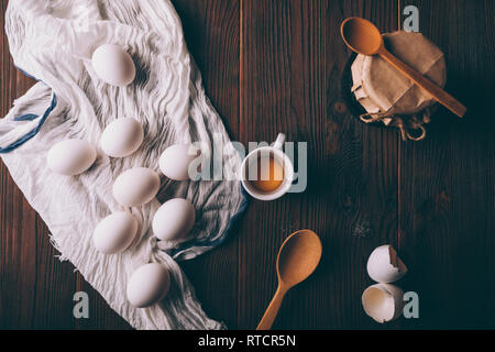 Rustic flat lay composition of ingredients and utensils for home baking. View from above on brown wooden table with eggs, yolk, shells, spoons and jar Stock Photo