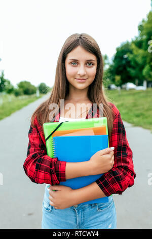 Girl schoolgirl teenager 10-15 years old, summer city after school lessons. In hands documents and notebooks notes. Happy smiling in city park Stock Photo