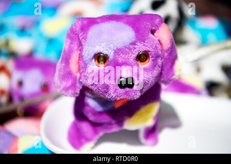 Close-up of one small super cute purple cored stuffed toy dog, standing on a white ground, with other toys out of focus in the background Stock Photo