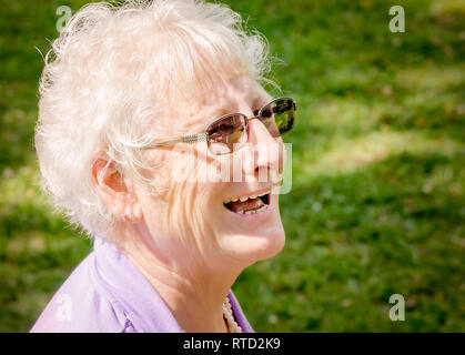 A mature woman wearing glasses smiles as she watches her daughter getting married at Marshall Park in Ocean Springs, Mississippi. Stock Photo