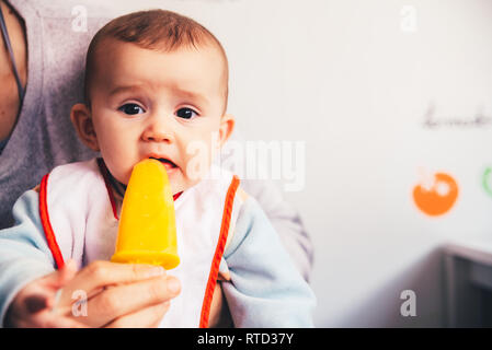 Baby savoring an orange ice cream. Stock Photo