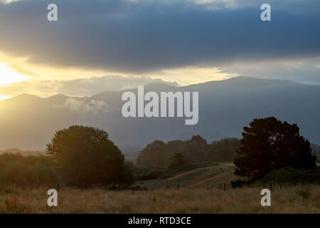 A dramtic sunset as the sun sets through clouds over the mountains near Waimate, New Zealand South Island Stock Photo