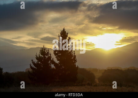 A dramtic sunset as the sun sets through clouds over the mountains near Waimate, New Zealand South Island Stock Photo