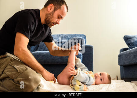 A father involved in taking care of his children by changing his daughter's dirty diaper. Concept of work family conciliation Stock Photo