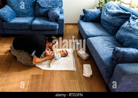 A father involved in taking care of his children by changing his daughter's dirty diaper. Concept of work family conciliation Stock Photo