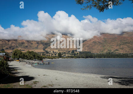 Pebble beach on Lake Wanaka on sunny summers day with clouds over the mountain peaks and blue sky New Zealand South Island Stock Photo