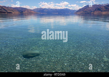 Beautiful Lake Hawea in summer blue sky clear water pebbles rocks clouds New Zealand South Island Stock Photo