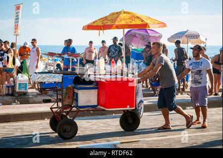 RIO DE JANEIRO - FEBRUARY 28, 2017: A Brazilian street vendor pushes a cart with sausages grilling to sell to crowds of young people at Carnival. Stock Photo