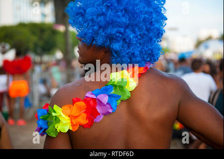 Close up of brightly colored rainbow flower lei and blue afro wig on unrecognizable man at a Brazilian Carnival street party in Rio de Janeiro, Brazil Stock Photo