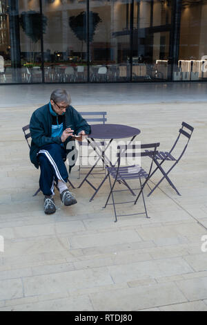 Man using a mobile sitting alone at a table in a courtyard near Kings Cross Railway Station, London, England Stock Photo