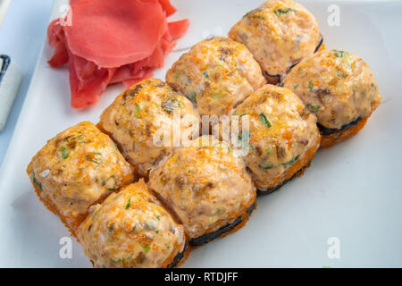 Baked rolls with scallop tar-tar, spicy sauce, cream cheese and mango with rice on white plate with gold border. Asian menu Stock Photo