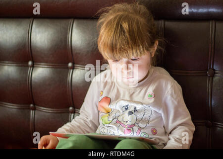 Little girl child plays with tablet pc and is watching Stock Photo