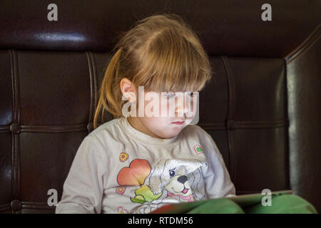 Little girl child plays with tablet pc and is watching Stock Photo