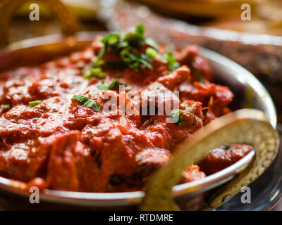 Indian Food or Indian Curry in a copper brass serving oriental bowl, pieces of chicken fillet in curry sauce ingredients in a pan with the old table Stock Photo