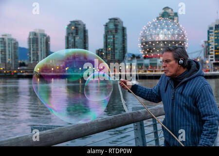 Downtown Vancouver, British Columbia, Canada - November 29, 2018: Man making big soap bubbles in False Creek during a vibrant sunset. Stock Photo