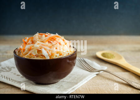 In a ceramic Cup on an old wooden table sauerkraut with carrots. Stock Photo