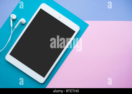 Flat lay of white tablet and earphones on blue, purple and pink background with copyspace. Stock Photo
