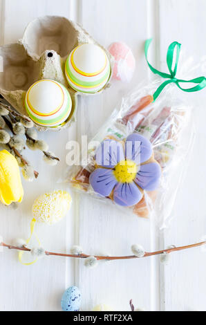yellow tulips, ginger cookies, willow twigs, decorative eggs in a tray laid out on a white old wooden table, easter holiday background with sweets, fl Stock Photo