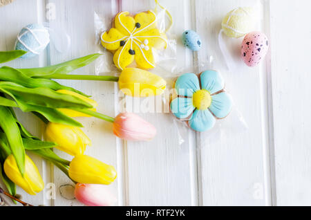 yellow tulips, ginger cookies, willow twigs, decorative eggs in a tray laid out on a white old wooden table, easter holiday background with sweets, fl Stock Photo