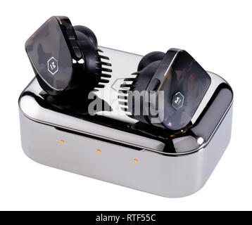 Master and Dynamic in ear earphones and charging case. Two earphones sitting on silver metal case that charges their batteries. Stock Photo