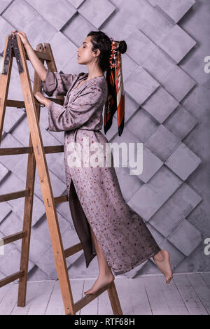 Prepossessing poser wearing dress standing on ladder during studio shooting Stock Photo