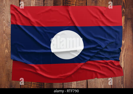 Flag of Laos on a wooden table background. Wrinkled Laotian flag top view. Stock Photo