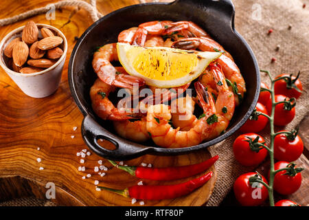 Spicy shrimp in a pan with garlic, cilantro and pepper, next ingredients for cooking, tomatoes on a wooden background Stock Photo