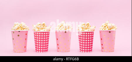 several cups of popcorn on a pink background Copy space Banner Stock Photo