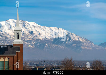 Church and homes against Mount Timpanogos and sky. Eagle Mountain, Utah landscape with view of a church and distant homes. The white peaked Mount Timp Stock Photo